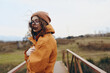 © SHOTPRIME STUDIO - Young woman lifestyle outdoors in autumn wearing orange jacket and knitted hat stands on wooden bridge with windy hair. Casual fashion and nature concept with relaxed mood and cool weather.
