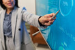 © pressmaster - Hispanic woman presenting data on large digital screen, holding pen and pointing at circular chart with percentage, engaging in business meeting or corporate presentation