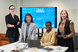 © pressmaster - Group of four businesswomen including Caucasian, Hispanic and Black women standing and sitting in modern office, smiling at camera, digital charts displayed on screen behind