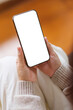 © Farknot Architect - Vertical mockup image of a woman holding and using mobile phone with blank desktop screen at home