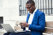 © Westend61 - Young businessman wearing blue suit jacket sitting on bench and using smartphone