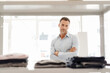 © Westend61 - Portrait of confident businessman standing at shelf with clothes
