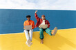 © VISTA by Westend61 - Friends sitting on colorful wall in Barcelona using laptops celebrating success
