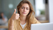 © Denis Yevtekhov - Exhausted woman at desk with thumb up showing burnout and approval, modern office workspace with laptop and charts, ironic workplace exhaustion, faceless tired worker, defocused background, with