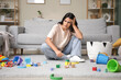 © Pixel-Shot - Tired young mother resting among scattered children's toys at home. Stress concept