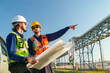 © FotoArtist - Two workers review blueprints at a construction site during the day with a clear sky