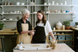 © AnnaStills - Senior Caucasian woman demonstrating pottery technique to young adult woman in ceramics studio, both standing at worktable with clay and sculpting tools visible
