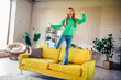 © deagreez - Happy young woman enjoying leisure at home while standing on a vibrant sofa in a bright and stylish interior space
