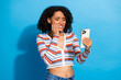 © deagreez - Young chic woman in striped cardigan on blue background looks at phone with worried expression