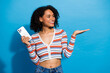 © deagreez - Young chic woman with phone smiling against a blue background wearing a striped cardigan