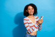 © deagreez - Young stylish woman smiling holding smartphone against blue background in striped sweater