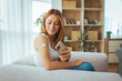 © Dragana Gordic - Woman Checking Glucose Monitor With Smartphone App While Relaxing On Couch At Home