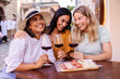 © Xavier Lorenzo - Three young women friends laughing at outdoor wine bar. Happy female friends sharing drinks and moments in a charming European street. Lifestyle and social concept.
