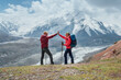 © Soloviova Liudmyla - Smiling each other backpackers couple with backpacks give high fives during Lenin peak ascent with mountain peaks in background. Extreme active people, high-altitude Pamir area mountaineering concept