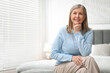© New Africa - Smiling senior woman in sweater on bed at home. Space for text