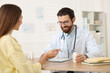 © New Africa - Woman having appointment with doctor at wooden desk in clinic