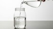 © pinto - Person pouring clear water from glass pitcher into mason jar on gray tabletop with white background