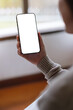 © Farknot Architect - Vertical mockup image of a woman holding and using mobile phone with blank desktop screen at home