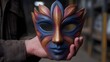 © Thares2020 - Vibrant ornate masquerade mask with floral details held by a hand in a dimly lit workshop