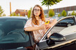 © maxbelchenko - Beautiful woman wearing glasses and holding phone stands next to car on sunny day. Young woman driver stands in a parking lot holding a phone. Concept of transportation, navigation. Lifestyle.