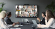 © fizkes - Group of businesspeople gather at conference table collaborating with multiple participants from diverse locations displayed on TV screen, take part in corporate discussion. Business virtual meeting