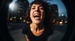 © 35mm STUDIO - Young woman with curly hair laughing and shouting in the city at night with fisheye effect.