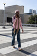 © wavebreak3 - African American female walking and talking on smartphone in plaza wearing pink hoodie and backpack