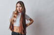 © SHOTPRIME STUDIO - Young woman with long hair wearing white crop top and black pants standing with hand on hip looking thoughtful on plain background.