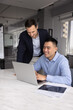 © fizkes - Supportive office mentoring. Smiling mid aged businessman mentor stand beside young male intern apprentice sitting by notebook offer guidance share insight give positive feedback on project solution