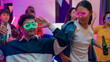 © tirachard - Diverse group multiethnic young adult Asia friend wear futuristic neon glowing glasses dance and drink alcohol beer fun hangout party in living room night indoor home. Disco lights illuminating house.