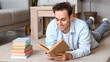 © Pixel-Shot - Young man reading book on floor at home