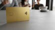© rangga - Golden Contactless Credit Card on Table with People Drinking Coffee in Background