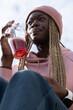 © wavebreak3 - African American woman holding plastic cup with red fizzy drink, wearing pink beanie and hoodie