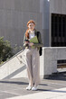 © wavebreak3 - Female student standing on campus holding green folder and phone wearing headphones and backpack