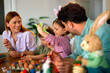 © djile - Girl showing painted easter egg to parents at table