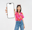 © sitthiphong - Portrait of young Asian woman in summer wearing floral shirt holding smartphone mockup of blank screen and smiling on white background.