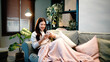 © Stella 16 - Smiling relaxed young woman sitting on couch covered by blanket using cell phone technology, happy lady holding smartphone, scrolling, looking at cellphone enjoying doing online