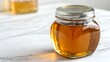 © Yura - Honey Jar on Marble SurfaceGlass Jar Filled with Golden Honey on Light BackgroundUnlabeled Honey Jar in Natural Soft Light
