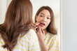 © Jestercine - Young woman looking into a mirror and pulling down her lower lip to check her gums or teeth. Concept of oral hygiene, dental health self-check, or mouth ulcer inspection.