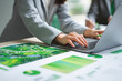 © Kowit - A person in business attire works on a laptop surrounded by green-themed charts and graphs, indicating data analysis or environmental planning.
