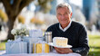 ©  VladaToday - Senior man enjoying a birthday picnic in a city park with gifts, flowers and cake for gift shop online campaign, outdoor party promotion and lifestyle marketing banner