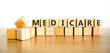 © Dzmitry - Medicare word symbol. Concept word Medicare on beautiful wooden blocks. Beautiful wooden table white background. Medical support help medicare word concept. Copy space.