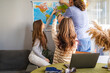 © Ina - Modern family active discussing and choosing travel destination at home, pointing at world map and discussing vacation plans together. Family travel planning and decision making concept.
