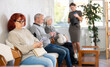 © JackF - Group of positive people of different ages holding mobile phone and chatting with friends during sitting in queue at hall of civil service building or big medical clinic