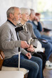 © JackF - Calm elderly man sitting in clinic waiting area with other senior patients in background