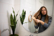 © Zoran Jesic - Woman brushing long hair in bathroom mirror, daily self-care routine