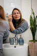 © Zoran Jesic - Woman applying eyebrow pencil in bathroom mirror for beauty routine