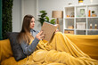 © Zoran Jesic - Woman relaxing at home reading book wrapped in blanket