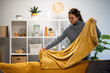 © Zoran Jesic - Woman folding yellow blanket on living room couch