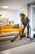 © Zoran Jesic - Young woman vacuuming rug in modern living room